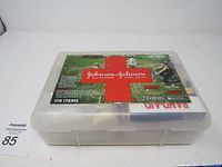 Top and angled view of the Johnson & Johnson All-Purpose First Aid Kit in a clear plastic box with outdoors-themed label showing brand names and kit contents.