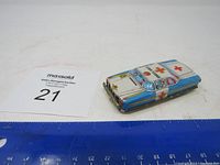 Photo of the vintage tin ambulance toy car with a ruler for scale, showing the side and part of the roof decoration