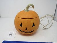 Orange pumpkin shaped electric decoration with jack-o-lantern face and power cord visible