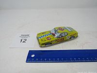 Yellow tin race car with ruler for size reference showing approximately 6 inch length.