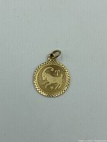 Front view of round gold pendant with Taurus symbol and decorative border.