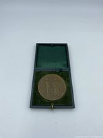 Bronze medal viewed inside the presentation case from angle showing medal and green velvet lining