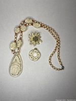 Full view of necklace, carved circular pendant, and floral brooch arranged on gray surface