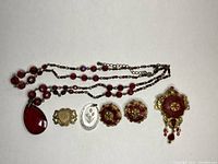 Top-down view of all jewelry items showing necklace, brooches, pendants and earrings arranged on white background