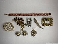 Assorted vintage jewelry pieces including a rhinestone bracelet, various brooches with different shapes and colored rhinestones, one dangle earring, and a pair of clip-on pearl earrings.