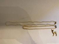 Photo showing two pearl necklaces and gold-tone deer brooch laid flat, with shadows and color variations visible on beige surface.