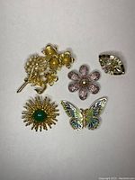 Five assorted vintage brooches shown on a neutral background, with visible details and condition