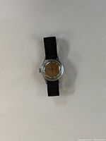 Front view of vintage wristwatch with black fabric strap, round metal case, and aged dial