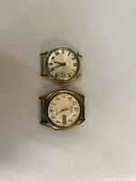 Top and bottom views of two vintage wristwatch cases without straps; one with Roman numerals dial, one with Arabic numerals and day-date display.