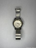 Front view of watch showing silver dial, applied hour markers, date window at 3 o'clock and attached expansion band