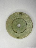 Top view of carved round stone pendant highlighting floral and abstract carved details with central hole