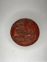 Top view of round cinnabar box lid showing raised carved landscape with mountains and trees.