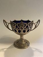 Front and side angle view of cobalt blue glass chalice with silver floral overlay and handles on both sides