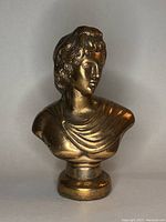 Front view of the copper bust showing the figure's detailed hair, face, and draped clothing on a cylindrical base.