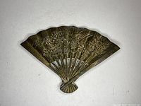 Front view of a vintage decorative metal fan showing embossed floral design