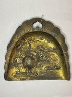 Photo showing the front side of the metal dustpan with detailed crane and landscape engraving in brass-like finish.