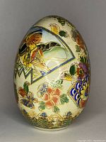 Photo of the egg-shaped Satsuma porcelain vase showing one side with detailed floral and leaf patterns in bright colors with gold accents on a cream crackle glaze background.