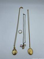 Full view of three gold fill lockets on chains, gold-tone ring, and two black pendant necklaces with charms.