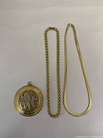 Chunky link chain necklace and flat herringbone chain necklace alongside round monogram pendant shown on white background