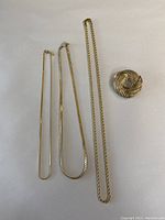 All four jewelry pieces together on a white background: three gold tone necklaces of varying styles and one knot-style brooch.