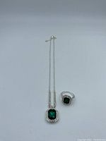 Photo of the vintage jewelry set showing necklace with green rectangular stone pendant and matching ring with green stone, both in silver-tone metal with clear stone borders.