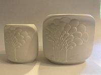 Both vases side by side showing size difference and embossed floral designs on white ceramic.