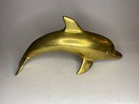Front and side view of vintage gold-tone metal dolphin statue showing smooth contours and slight surface wear.