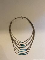 Full front view of necklace arranged flat showing multi-strand liquid silver tubes with turquoise bead decoration.