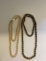 Two necklaces side by side on a white background: pearl necklace with silver clasp and unakite bead necklace.