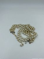 Pearl necklace loosely coiled, showing pearls and metal clasp with hook component.