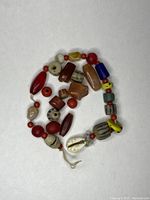 Photo showing a coiled string of various vintage trade beads on a white background, highlighting various bead shapes and materials including a cowrie shell.
