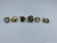 Front view of seven assorted vintage rings arranged in a row showing variety of stones and settings.