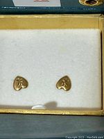 Close-up of pair of small gold heart shaped earrings with engraved star design on white padding.