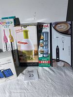 Front view of five assorted items showing their boxes and physical appearance including the ThermoPro monitor, kitchen chopper, T-fal ActiFry accessory, milk frother, and electric toothbrushes.