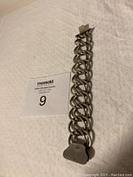 Full bracelet showing interlocking thick circular links and clasp lying on a white surface with auction tag.