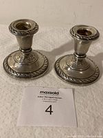 Pair of sterling silver candlesticks on white surface with identification card.