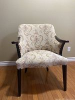 Front view of antique armchair showing floral upholstery and carved wooden arms.