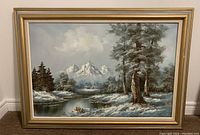 Full view of the framed oil painting showing a snowy mountainous landscape with trees and a lake.