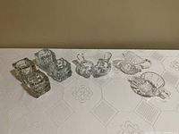 Photo showing all eight items arranged in line on white cloth background: three sets of votive candle holders and the crystal cream and sugar set.
