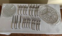Full set of cutlery and two glass serving dishes on white tablecloth, showing arrangement and condition