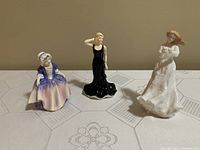 Three Royal Doulton porcelain figurines displayed together on table.