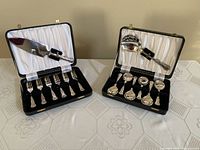 Two black lined serving flatware cases showing cake serving set with knife and forks, and fruit spoon set with spoons and ladle.