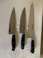 Three kitchen knives on a white textured tablecloth showing branding and handle style