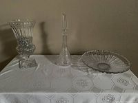 All three glass items displayed: large vase with glass marbles, vintage crystal decanter with stopper, and large shallow glass bowl on a white tablecloth.