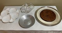 Four serving and fruit bowls displayed on tablecloth: cream leaf-shaped ceramic dish, silverplate serving dish with wooden insert, hand-forged fruit bowl, Waterford Marquis crystal bowl.