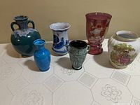 Photo of six vintage vases on table, including cranberry glass, Limoges, and two-handled green vase