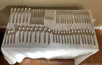 Top-down view of the complete 62-piece flatware set laid out on a table, showing spoons, forks, and cutters organized in rows.