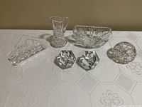 Full view of the six vintage crystal pieces on a white embroidered tablecloth: napkin holder, milk jug, candy/nut dish, votive candle holder, and two candlesticks.