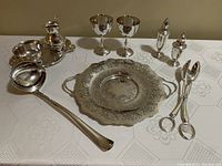 Full lot showing cream and sugar set on tray, two goblets, dessert plate, heavy ladle, salad tongs, and sterling salt and pepper shakers arranged on a white tablecloth.