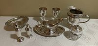 Front view of the entire set arranged on a table including goblets, candy dish, gravy boat with tray, small pitcher, salt and pepper shakers, and jam jar.